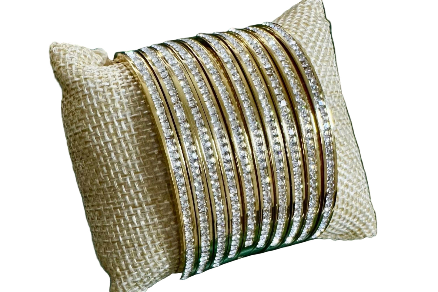 A collection of bangles with gold and silver colors, featuring zirconia stones, displayed on a burlap cushion.